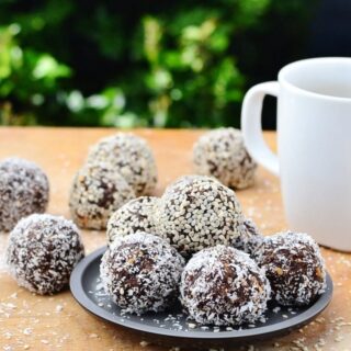 Side view of chocolate energy balls on black plate with white cup on wooden table.