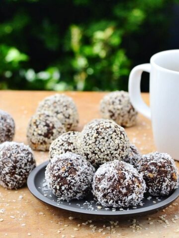 Side view of chocolate energy balls on black plate with white cup on wooden table.