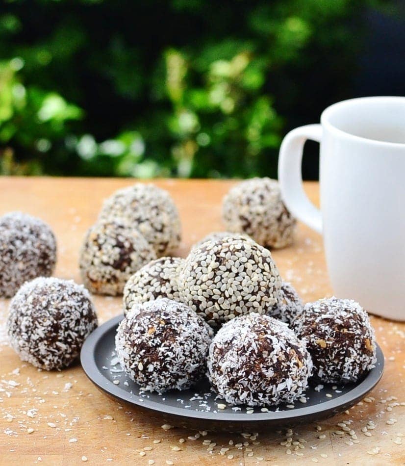 Side view of chocolate energy balls on black plate with white cup on wooden table.