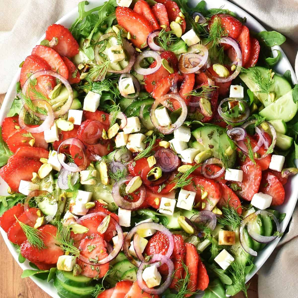 Close-up top down view of cucumber strawberry salad with feta and red onion on white plate.
