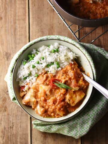 Tomato lentil fish stew with rice and spoon inside white bowl wrapped in green cloth.