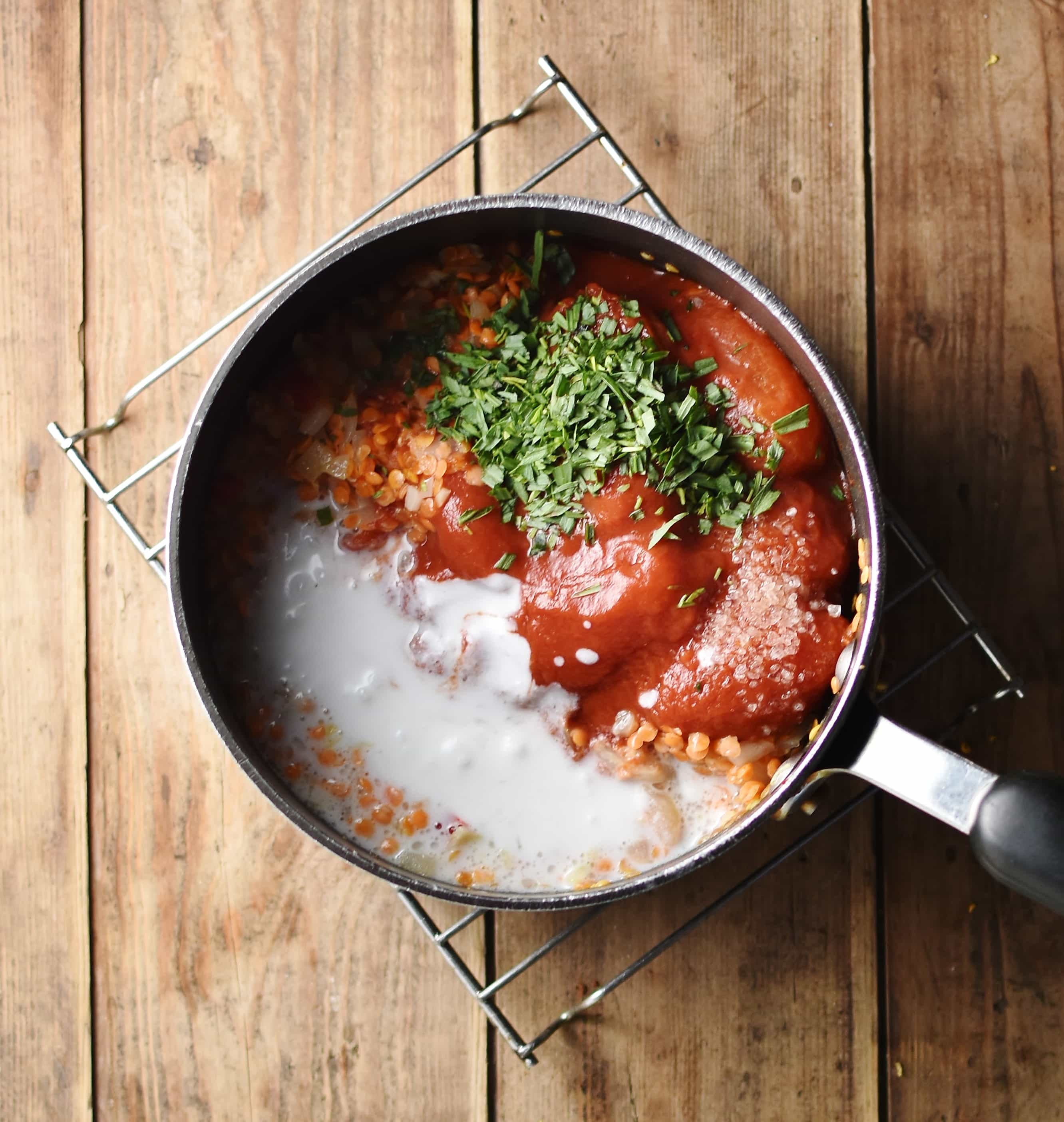 Tomatoes, coconut milk, red lentils and herbs inside large pot on top of cooling rack.