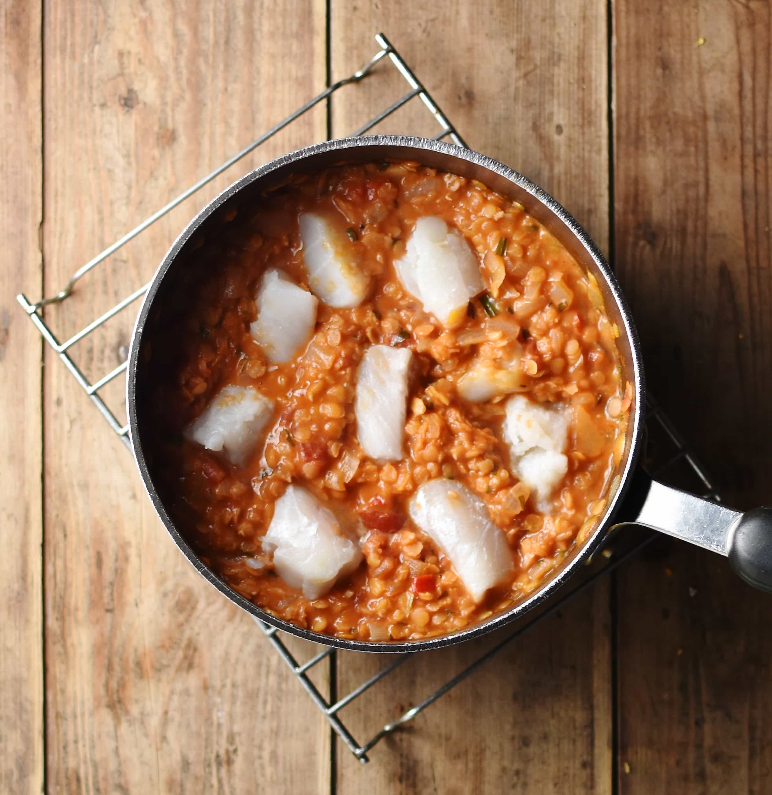 Red lentil stew with fish pieces inside large pot on top of cooling rack.