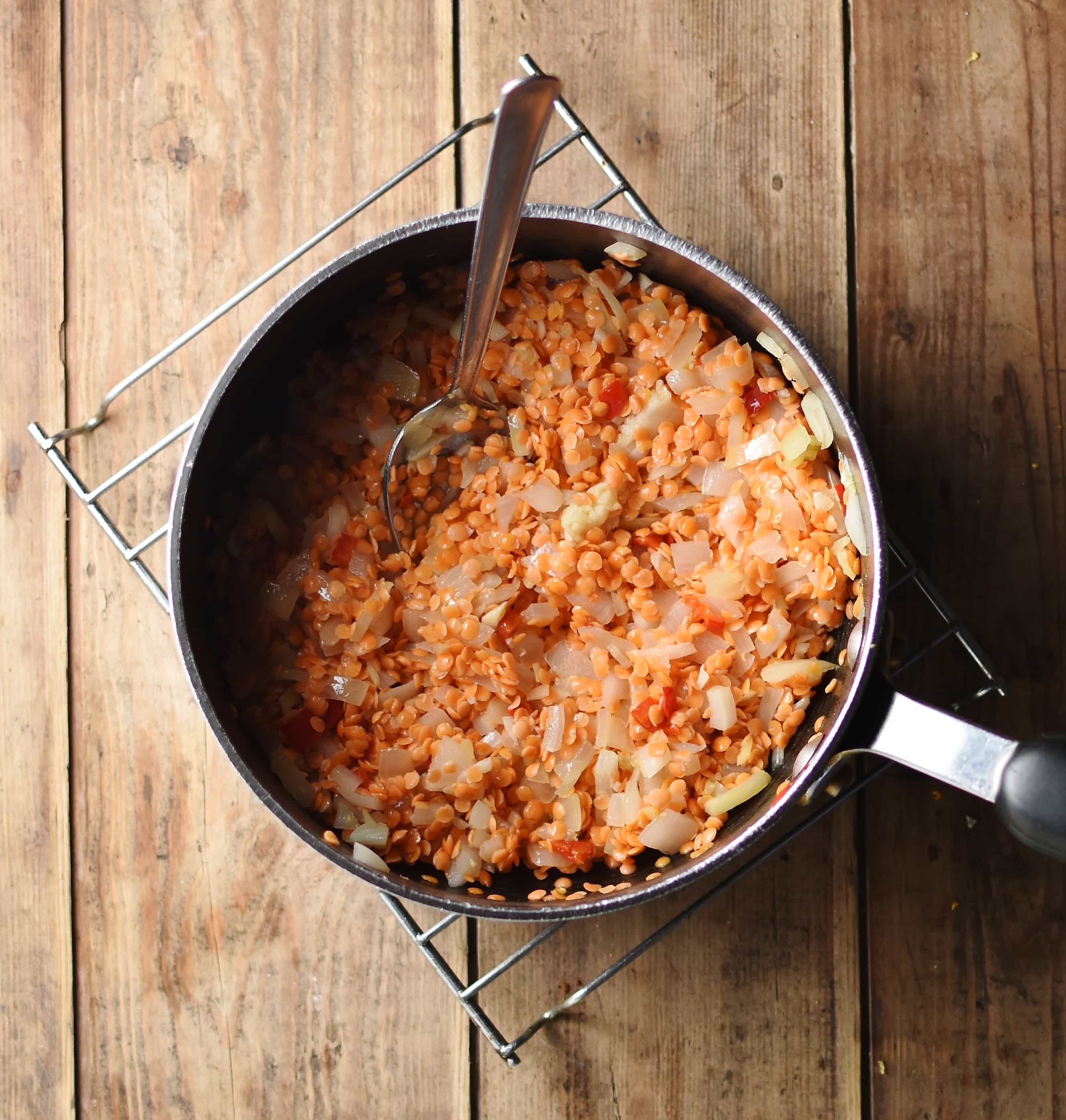 Fried onions and red lentils in large pot with spoon on top of cooling rack.