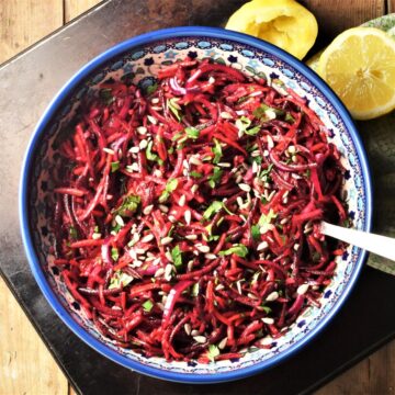 Beet slaw in large blue bowl with lemon in background.