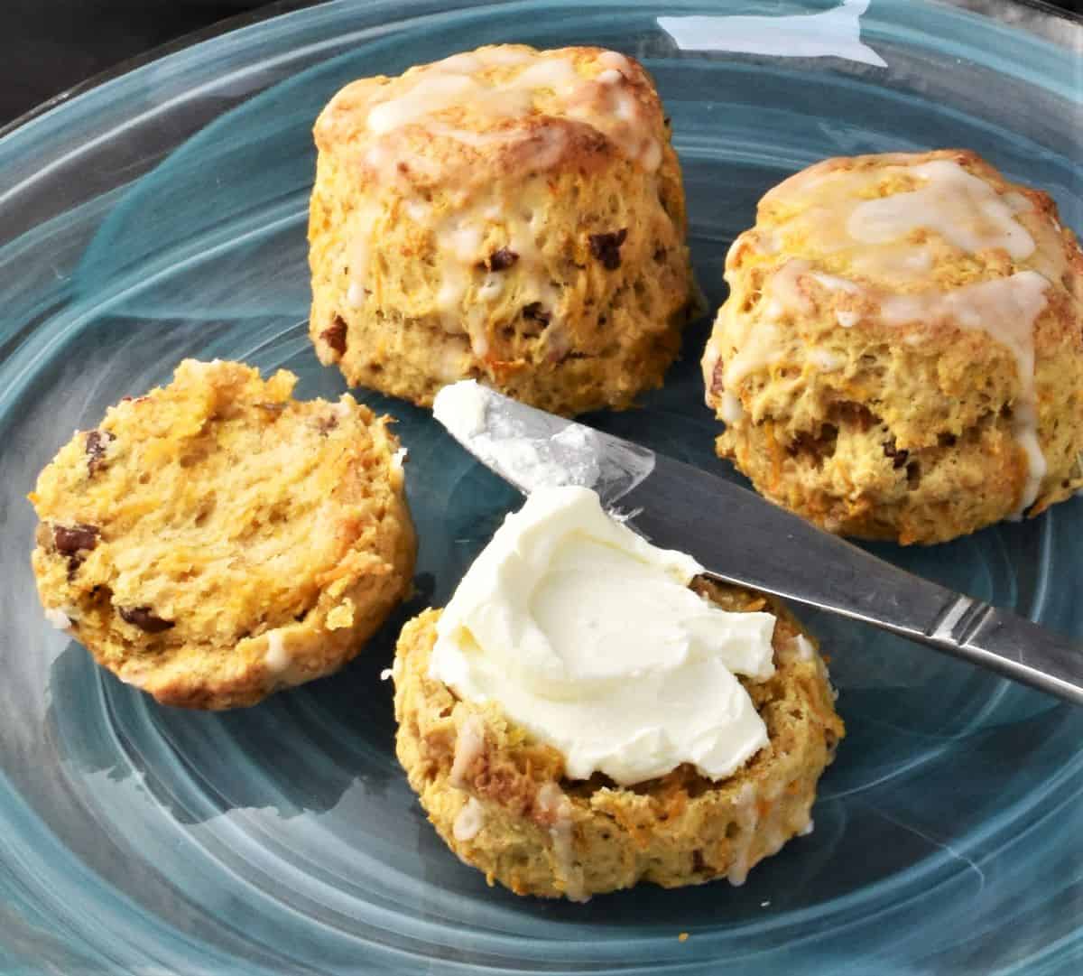 Side view of halved scone with cream cheese. knife and 2 more scones on top of blue plate.