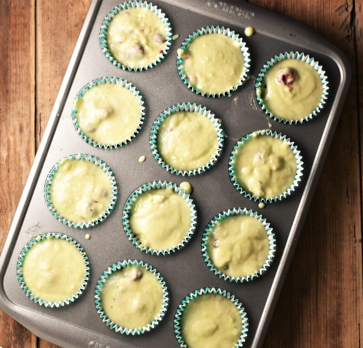 Muffin batter in 12 green muffin cases in pan.