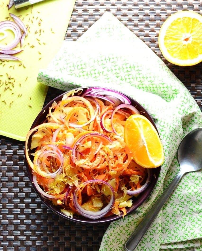 Top down view of Polish sauerkraut salad in purple bowl with orange, green cloth and partial view of yellow board.