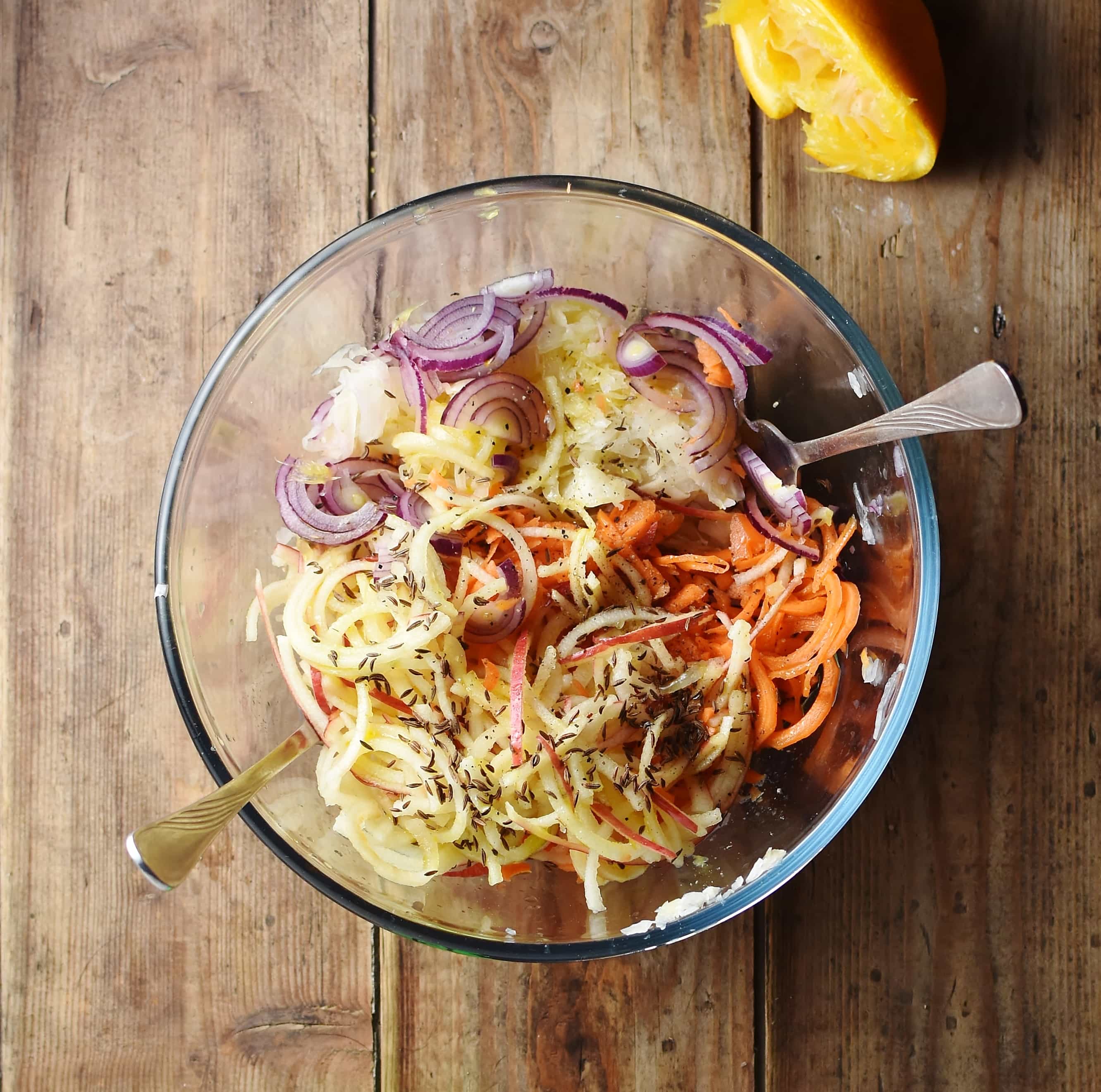 Spiralized carrot and apple, sliced red onion, spices and sauerkraut in mixing bowl with 2 forks.