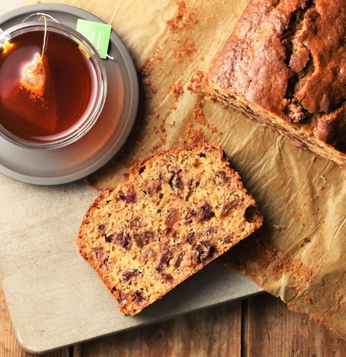 Slice of tea loaf cake, rooibos tea and partial view of tea cake on top of parchment.