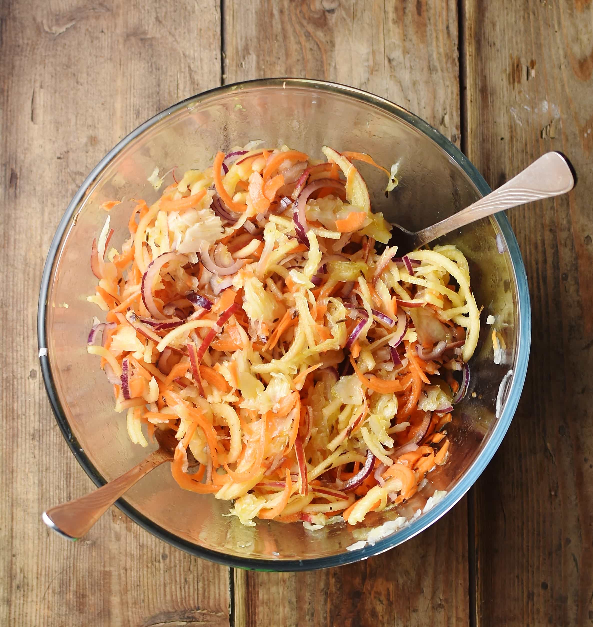 Sauerkraut, apple and carrot salad in mixing bowl with 2 forks.