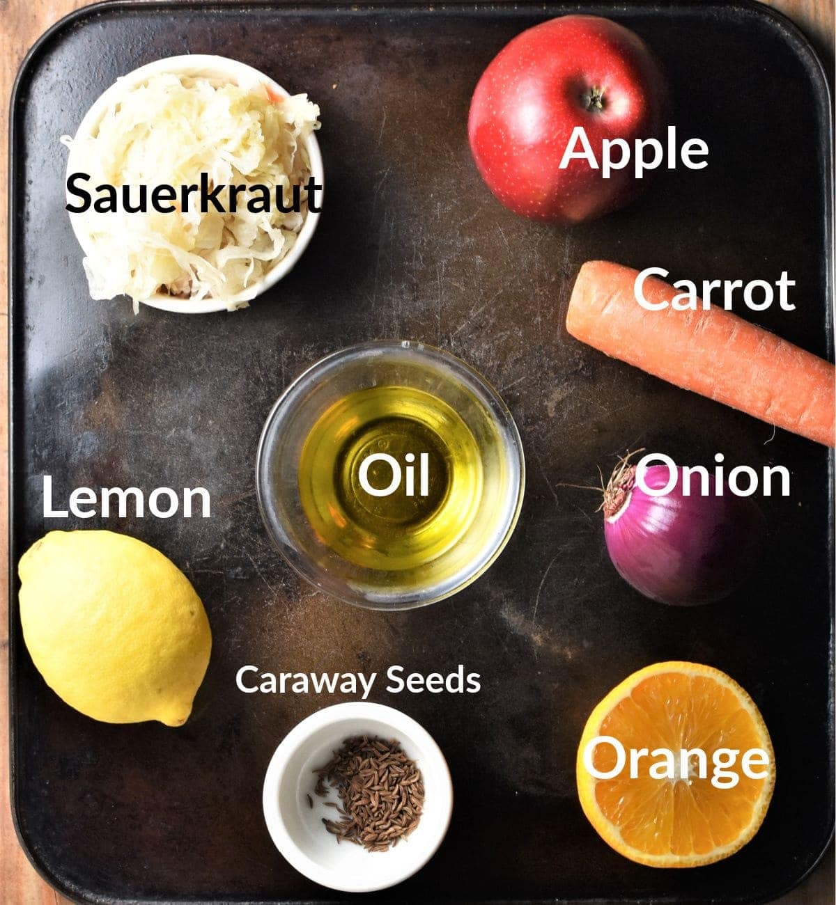 Sauerkraut salad ingredients on top of black tray and in individual dishes.