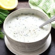 Side view of creamy cottage cheese ranch dressing in speckled bowl with spoon on top of saucer.