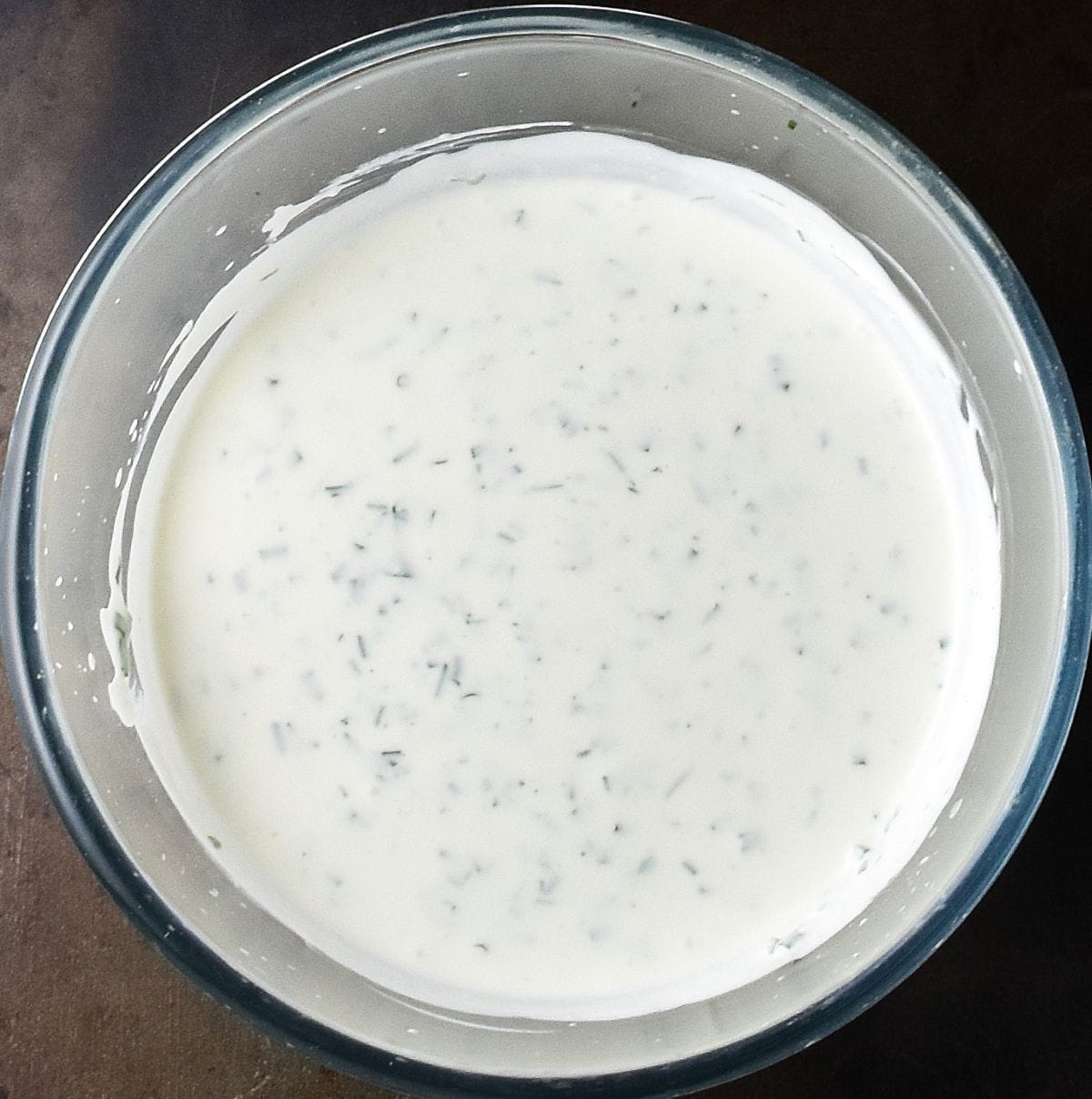Top down view of creamy ranch with cottage cheese speckled with herbs in glass bowl.