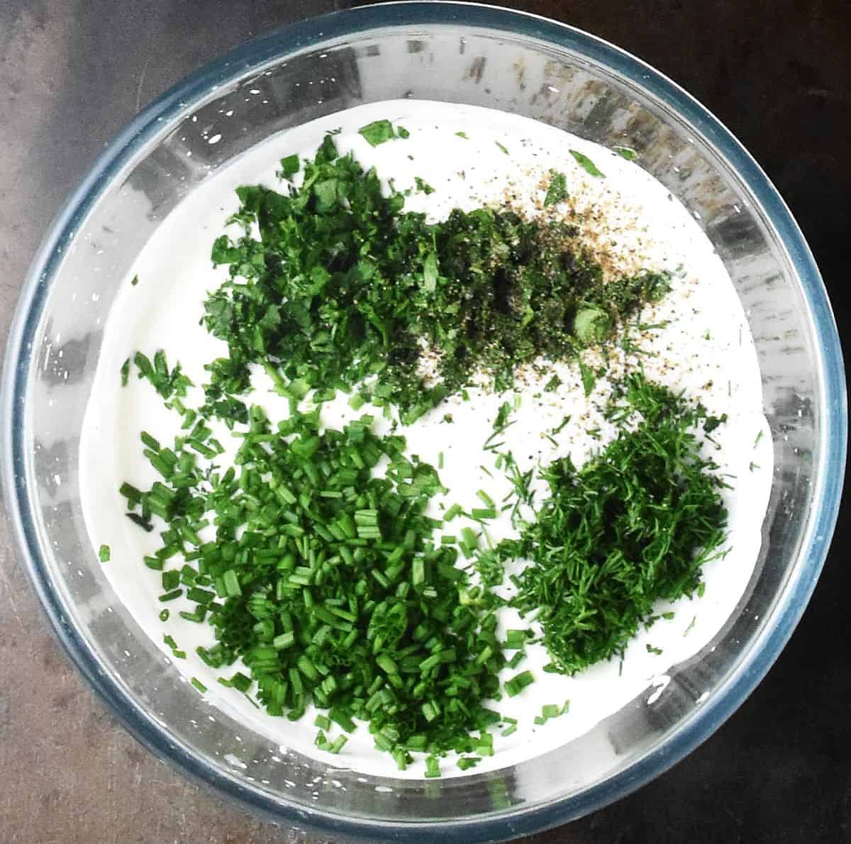 Creamy dressing with finely chopped fresh herbs on top in glass bowl.