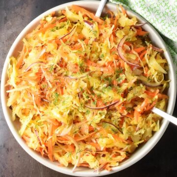Top down view of sauerkraut salad in white bowl with 2 spoons.