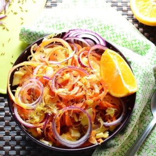 Top down view of sauerkraut carrot salad in purple bowl with orange, green cloth and partial view of yellow board.