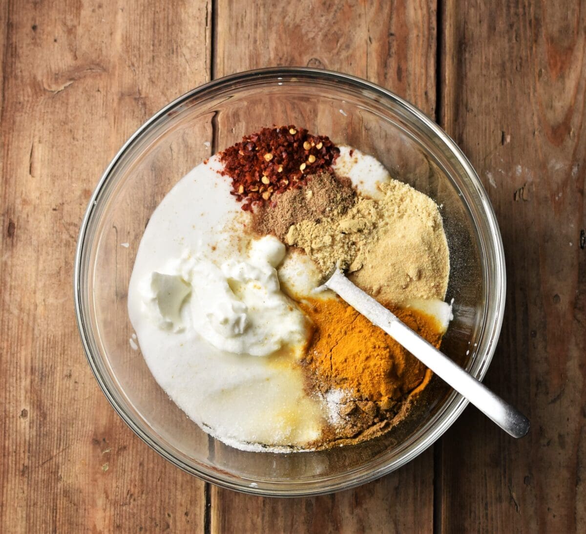 Yogurt and spices in mixing bowl with spoon.