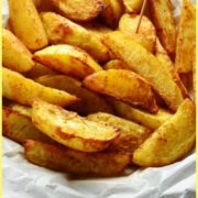 Spiced crispy potato wedges with cocktail sticks on white paper.