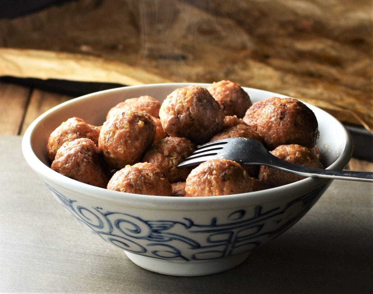 Side view of meatballs in white bowl with fork.