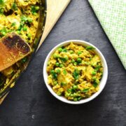 Top down view of curried chicken rice casserole in black oval dish on top of wooden board, with wooden spoon in bottom right corner.