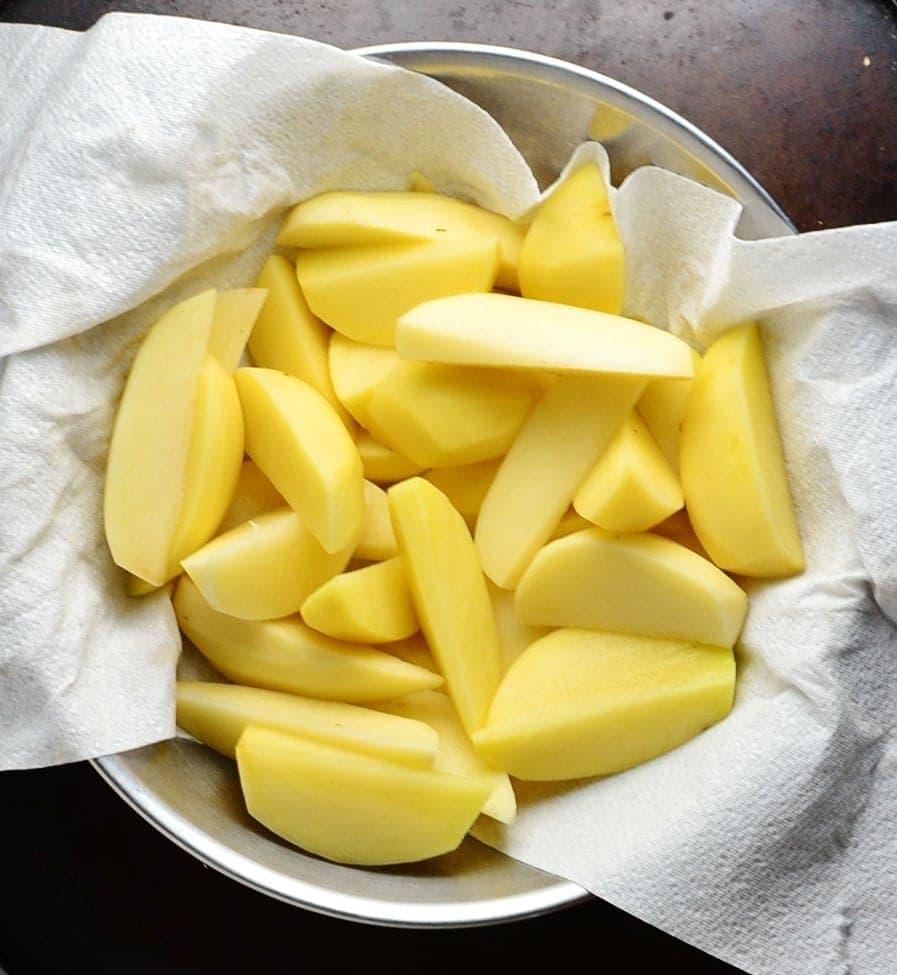 Raw potato wedges in metal bowl lined with paper towel.