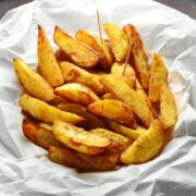 Spiced crispy potato wedges with cocktail sticks in basket lined with white paper.