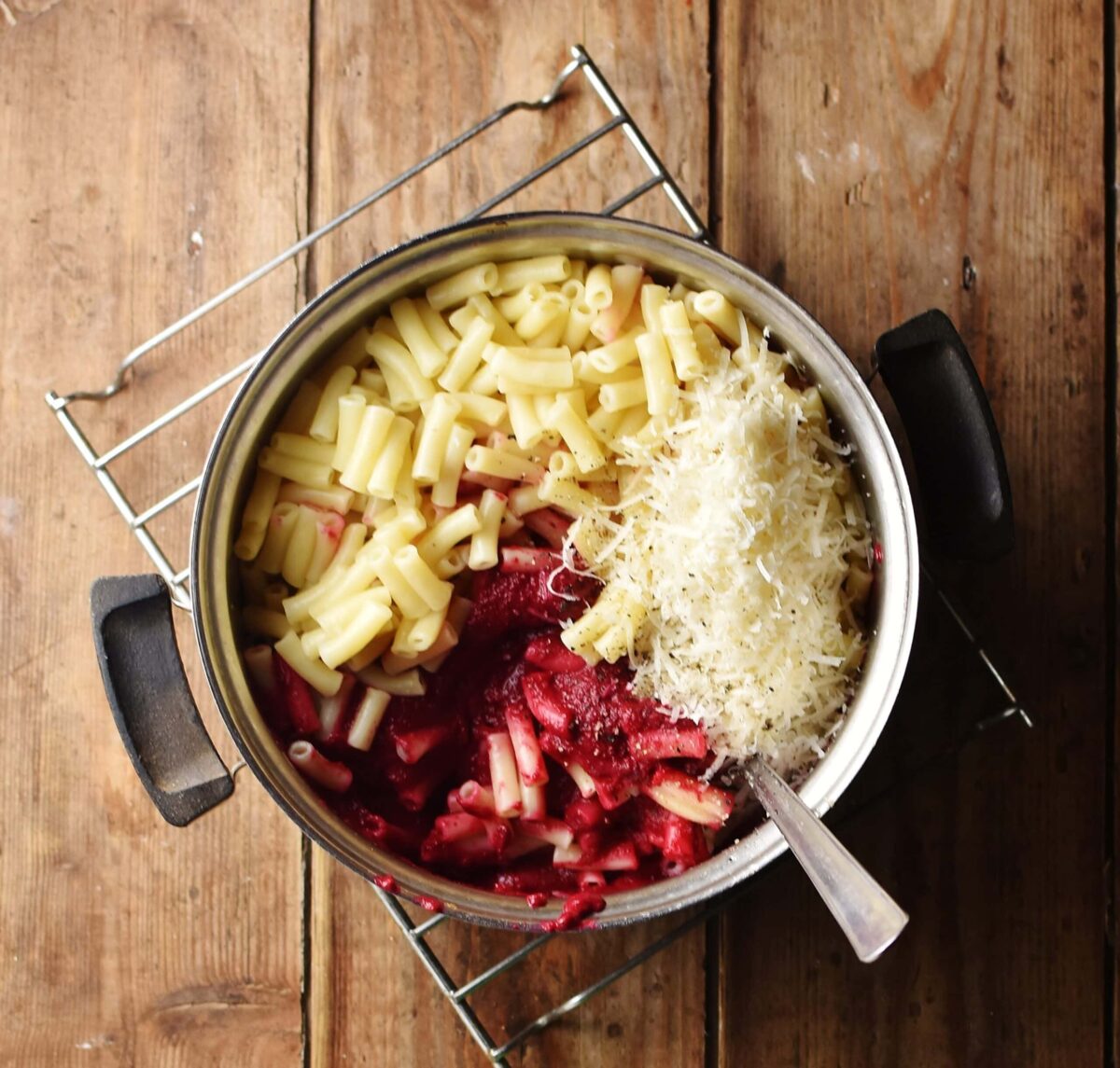 Macaroni, beet sauce and grated cheese in pot with spoon.