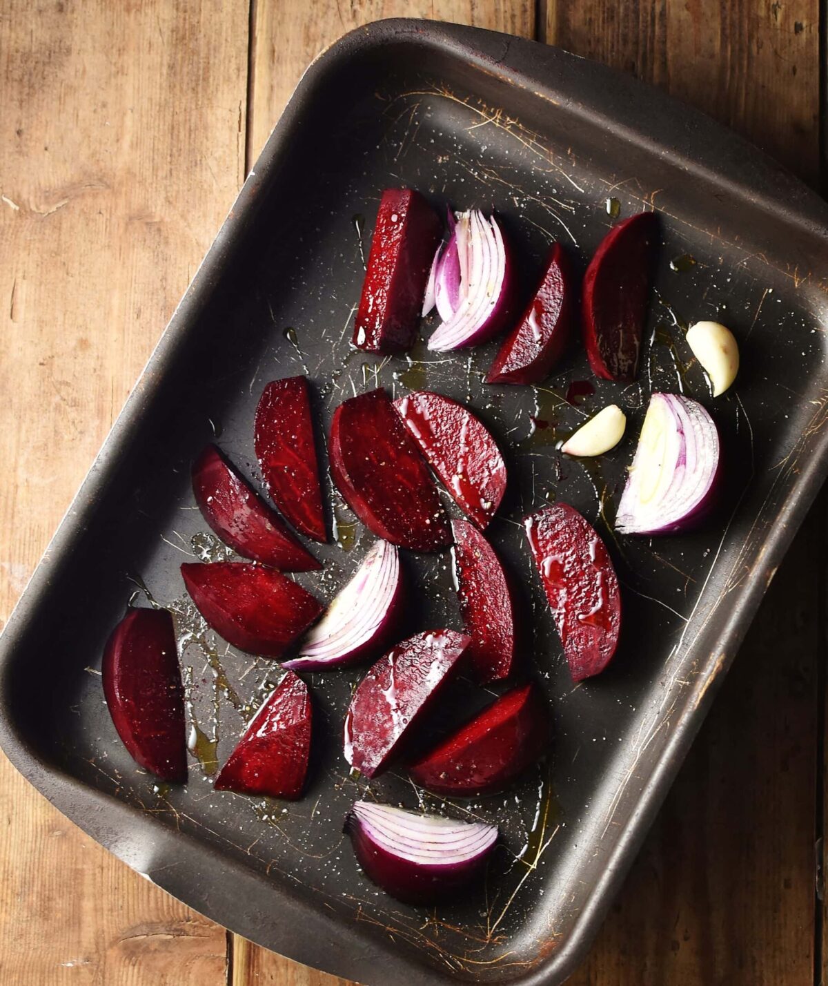 Beet wedges and red onion wedges with 2 garlic cloves in tray.