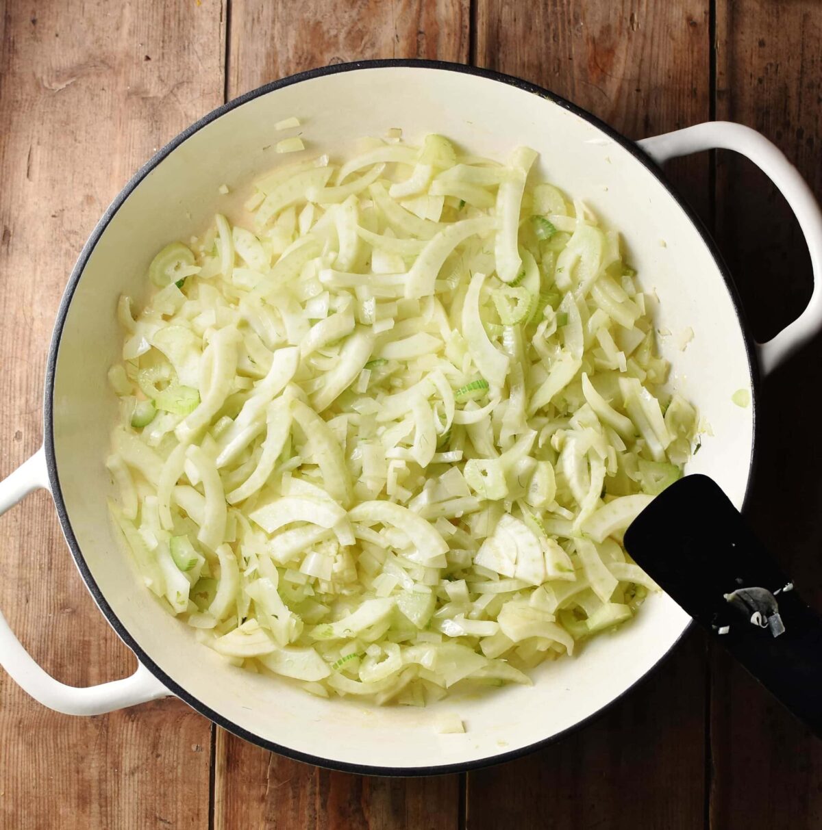 Sliced fennel and onions in large, white shallow dish with black spatula to the right.