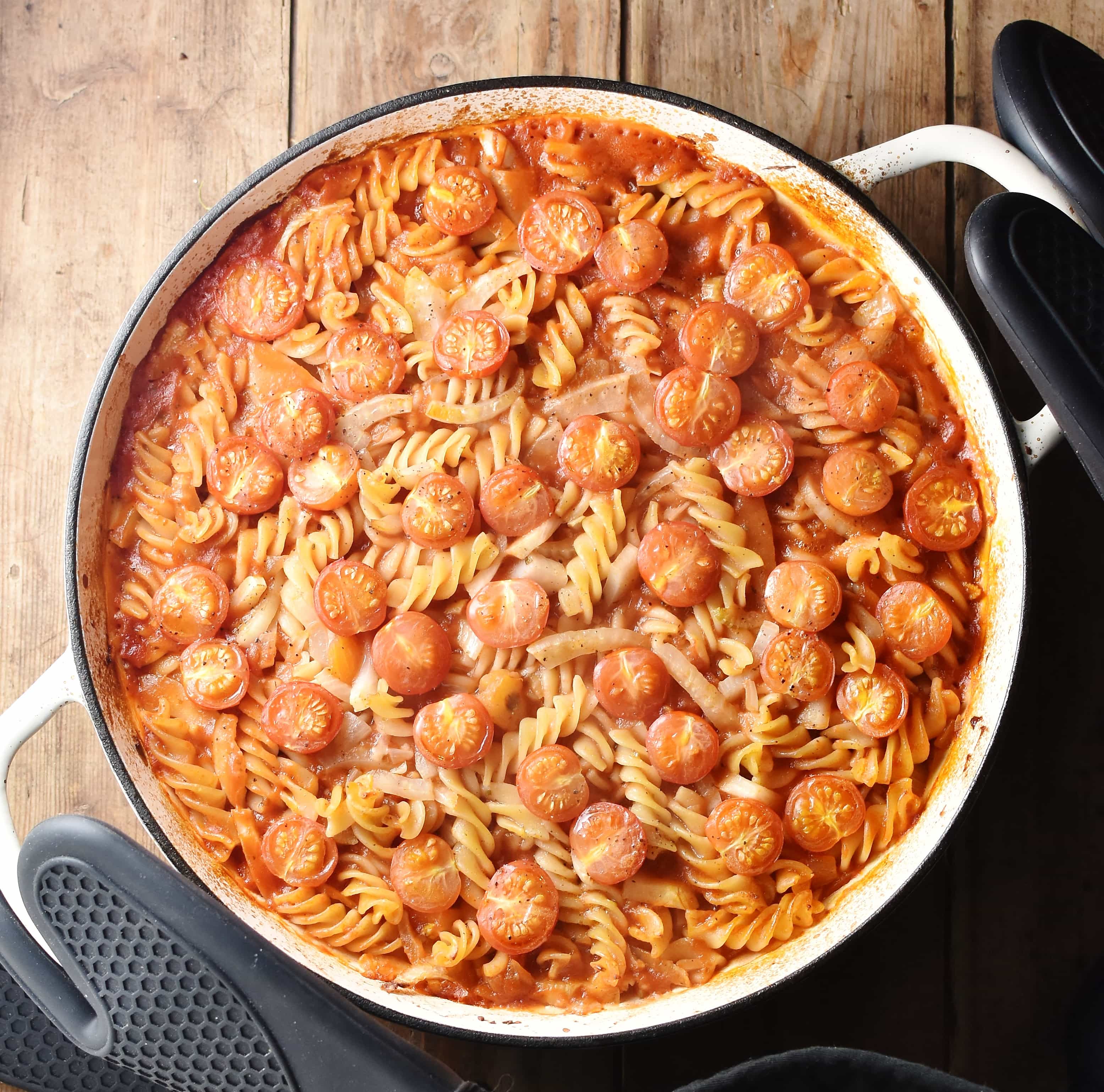 Baked tomato fennel pasta in large white casserole dish with black rubber gloves around handles.