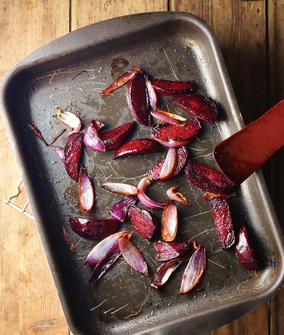 Roasted beetroot and red onion wedges in tray with red spatula.