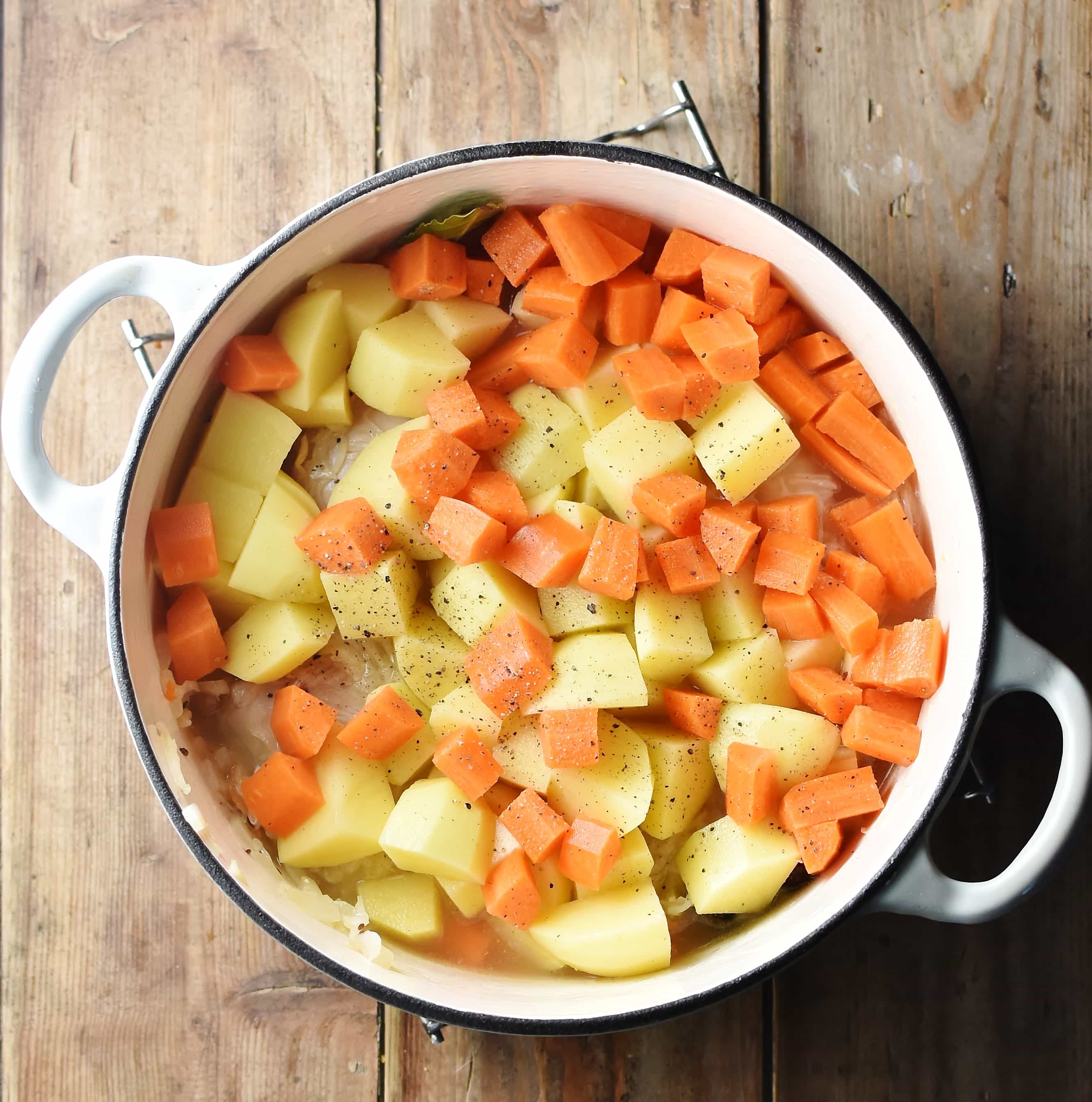 Cubed potatoes and carrots in large white pot.