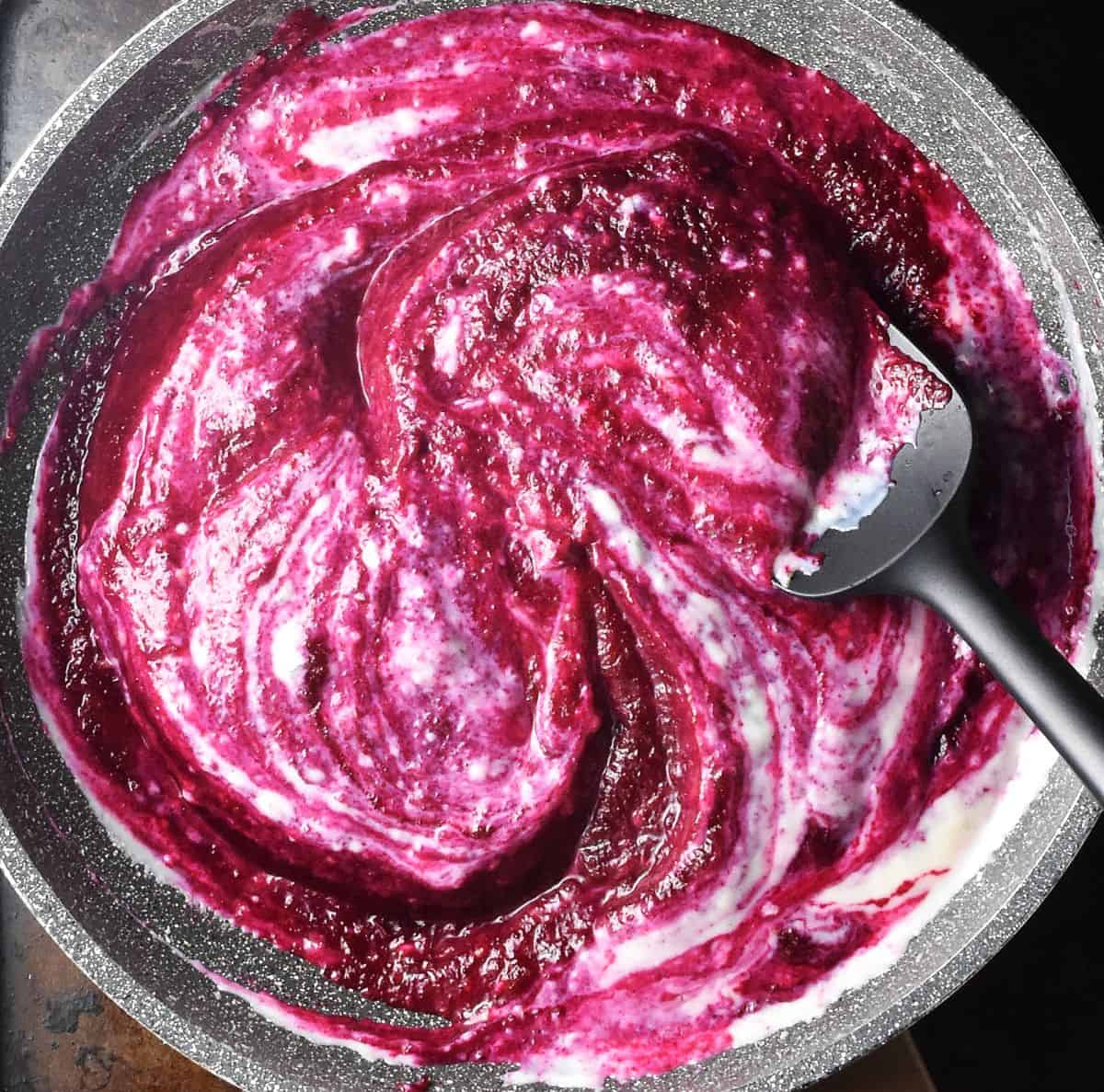 Marbled pink beet and white sauce in large pan with black spoon.