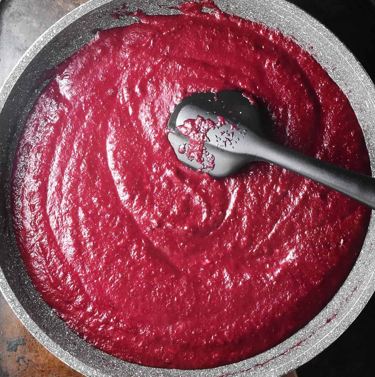 Creamy beet sauce in large, shallow pan with black silicone spatula.