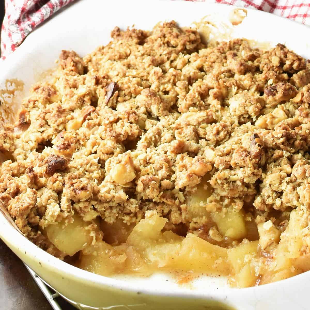 Close-up side view of healthy apple crumble in white ceramic dish.