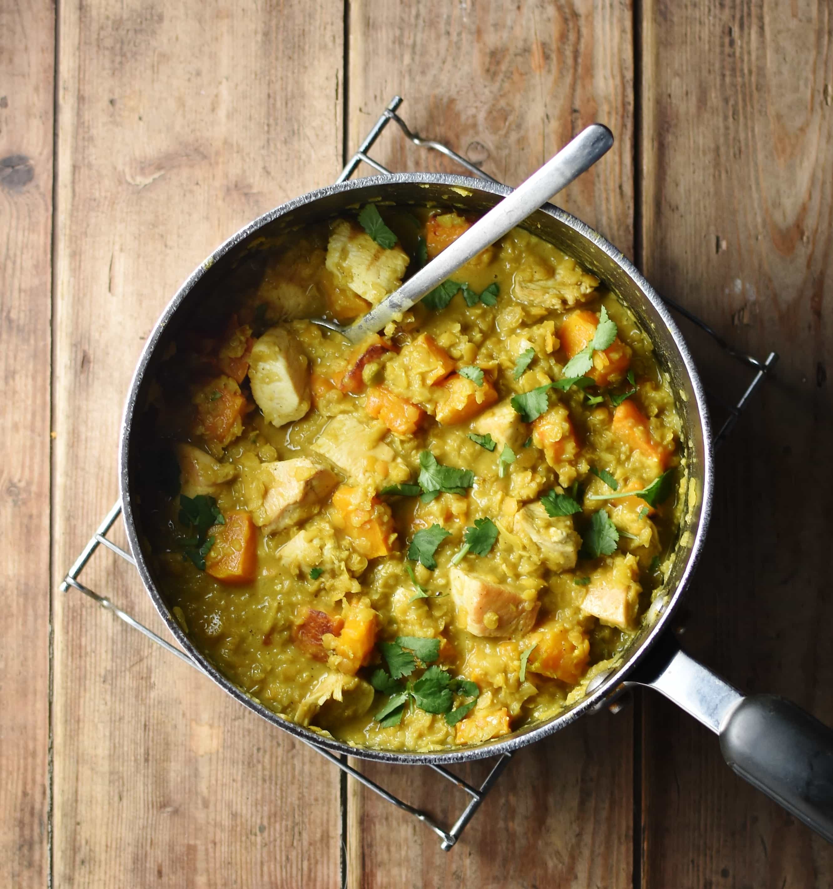 Chicken butternut squash curry with vegetables in large pot with spoon.