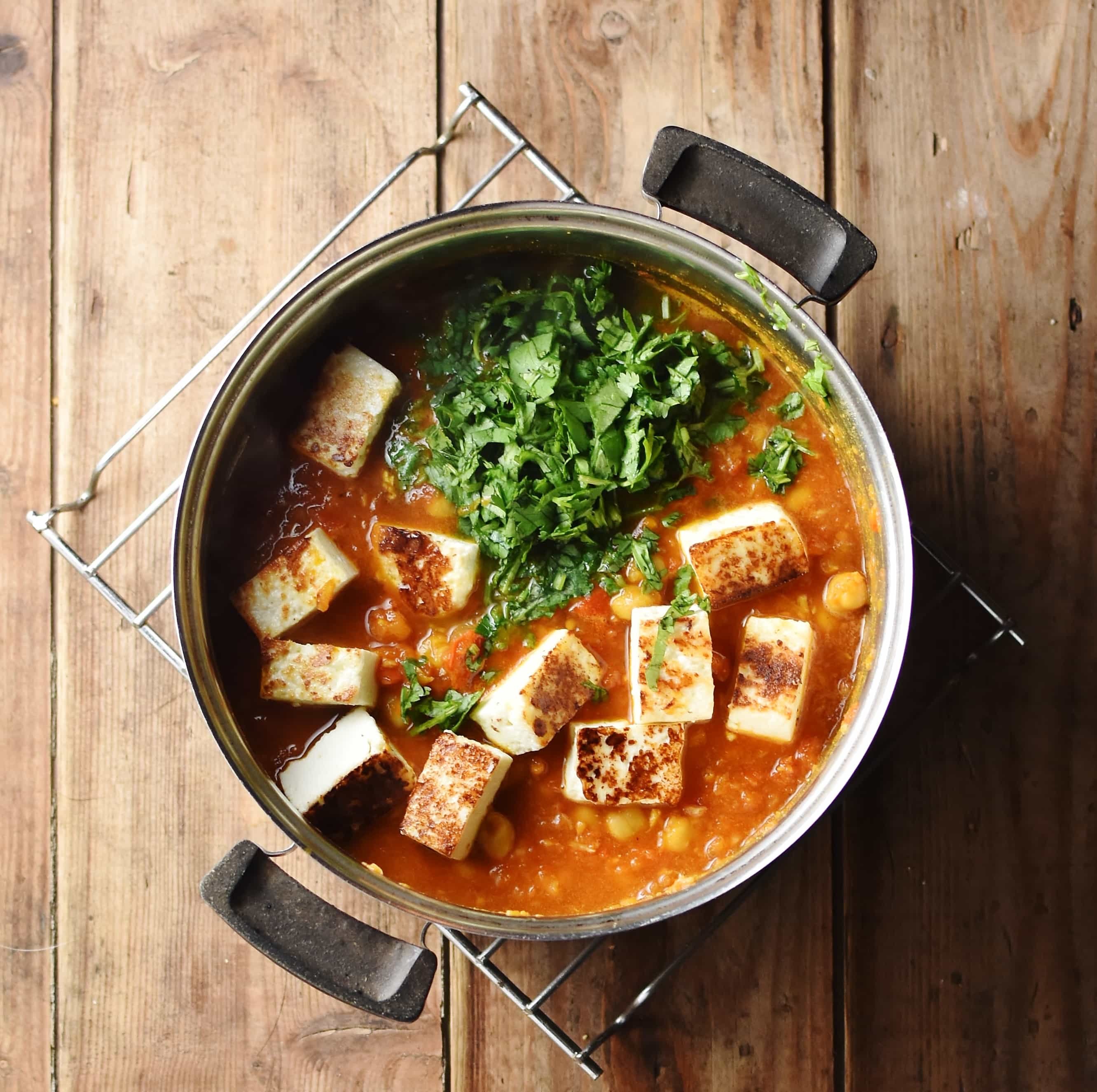 Tomato sauce with fried pieces of paneer cheese and chopped herbs in pot.