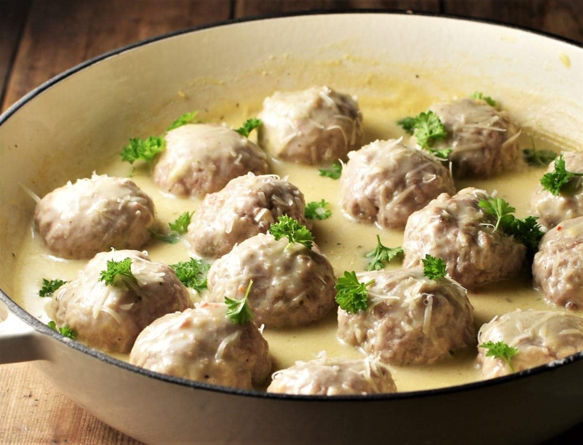 Side view of meatballs in creamy sauce with parsley in large white shallow dish.