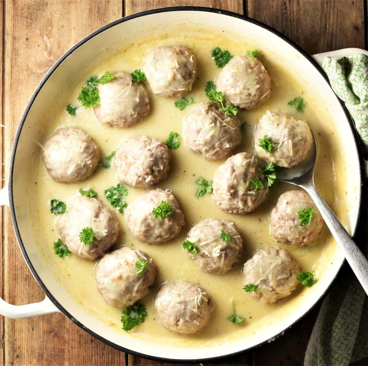 Meatballs in white sauce with spoon in large shallow dish.