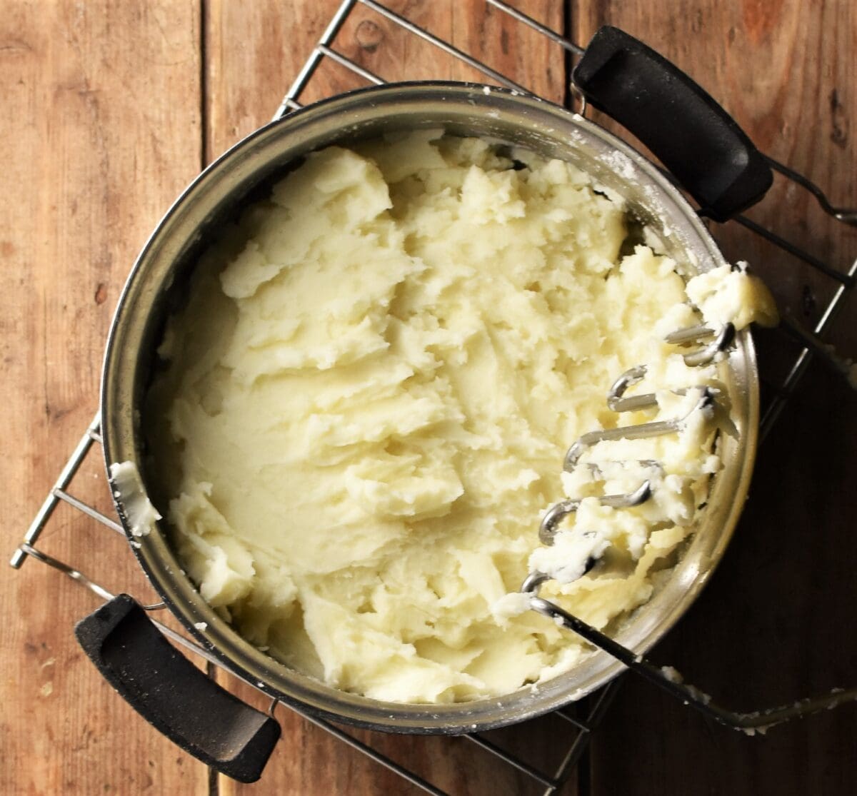 Potato mash in pot with potato masher to the right.