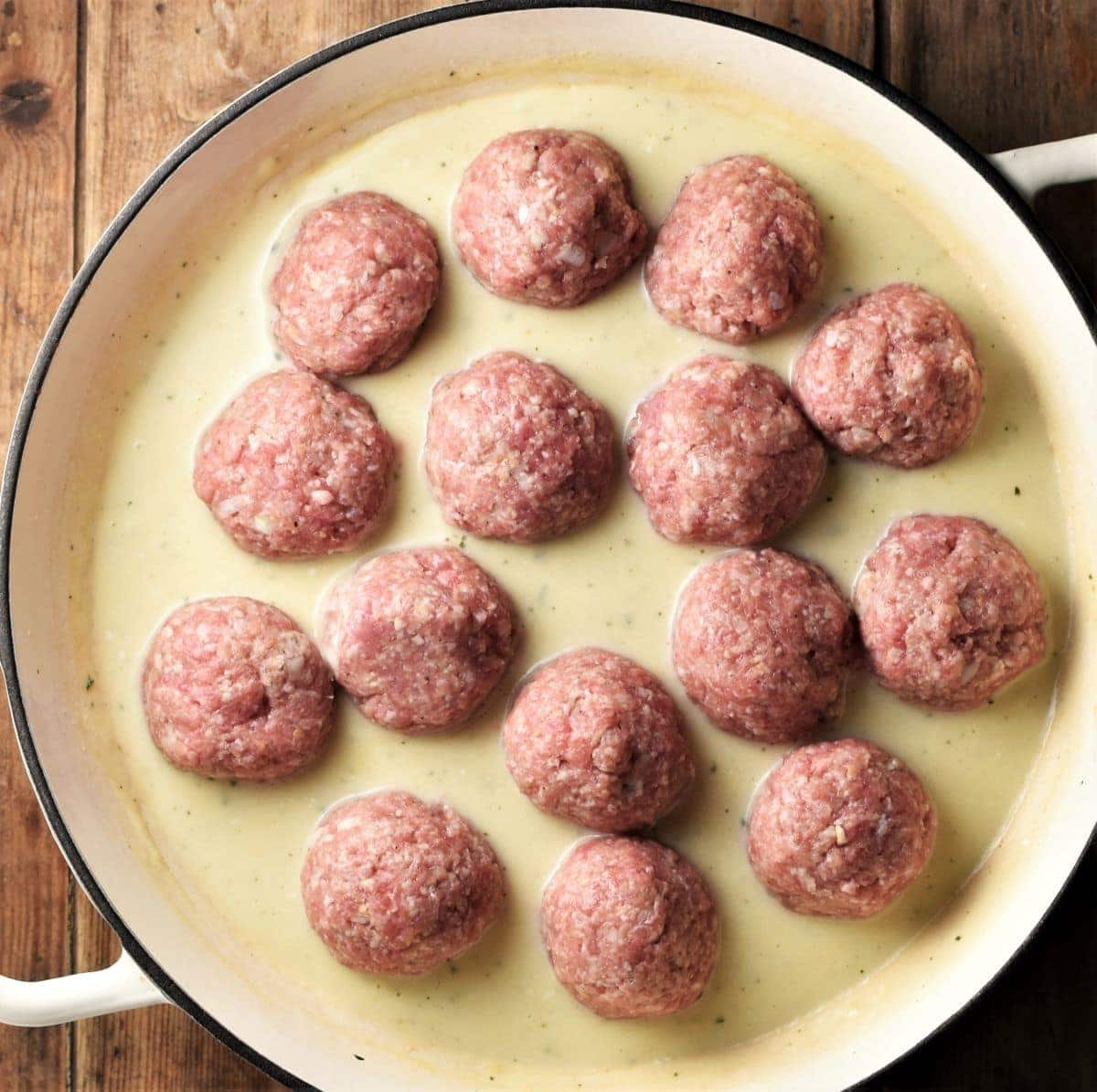 Raw meatballs in white sauce in large shallow pan.