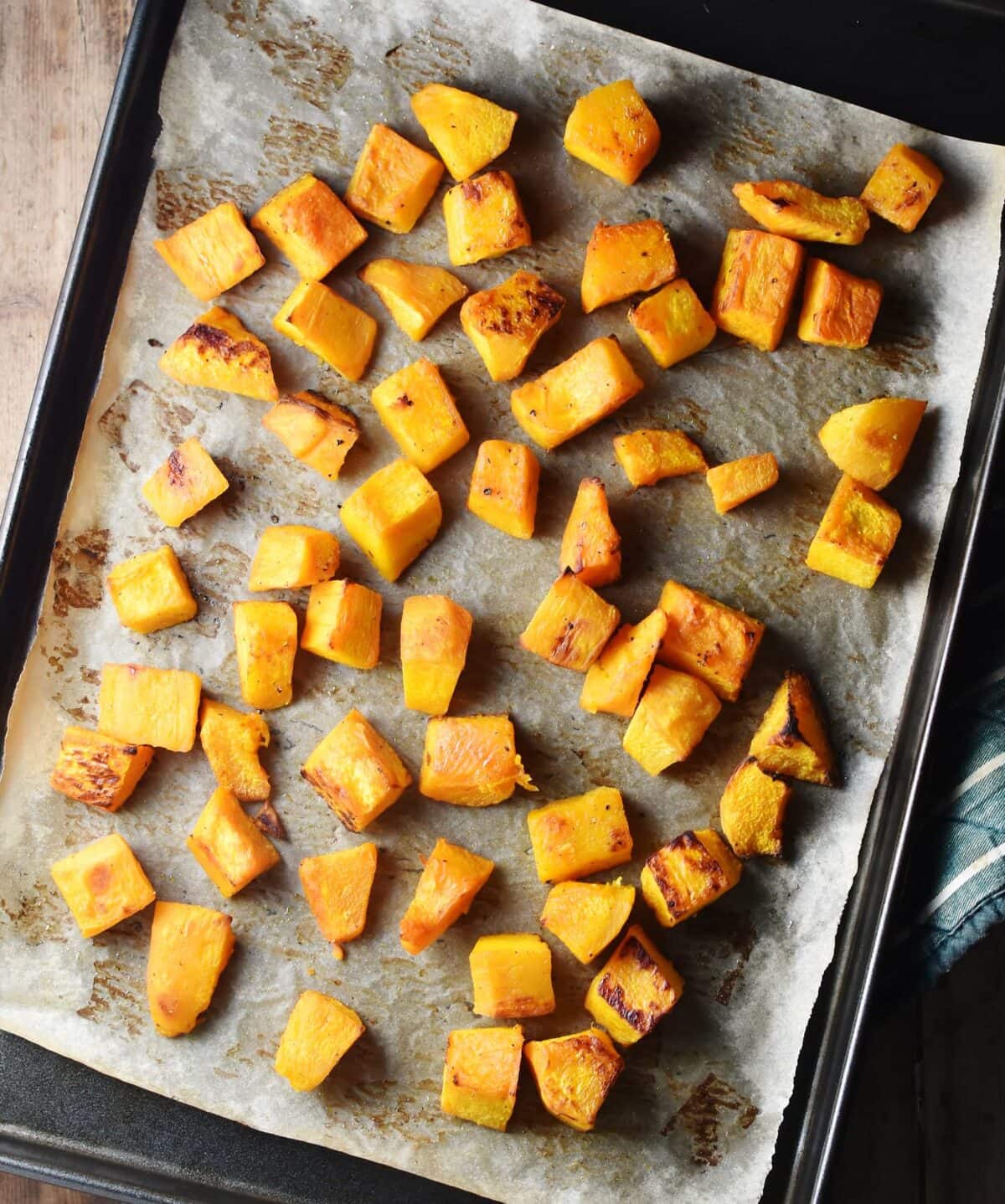 Roasted pumpkin cubes on top of baking sheet lined with parchment paper.