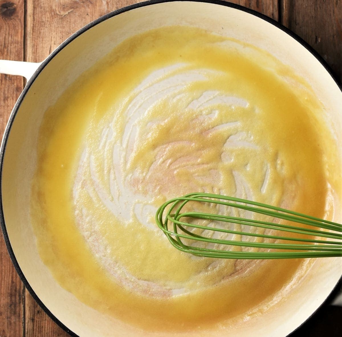 Roux mixture in large white shallow pan with green whisk.