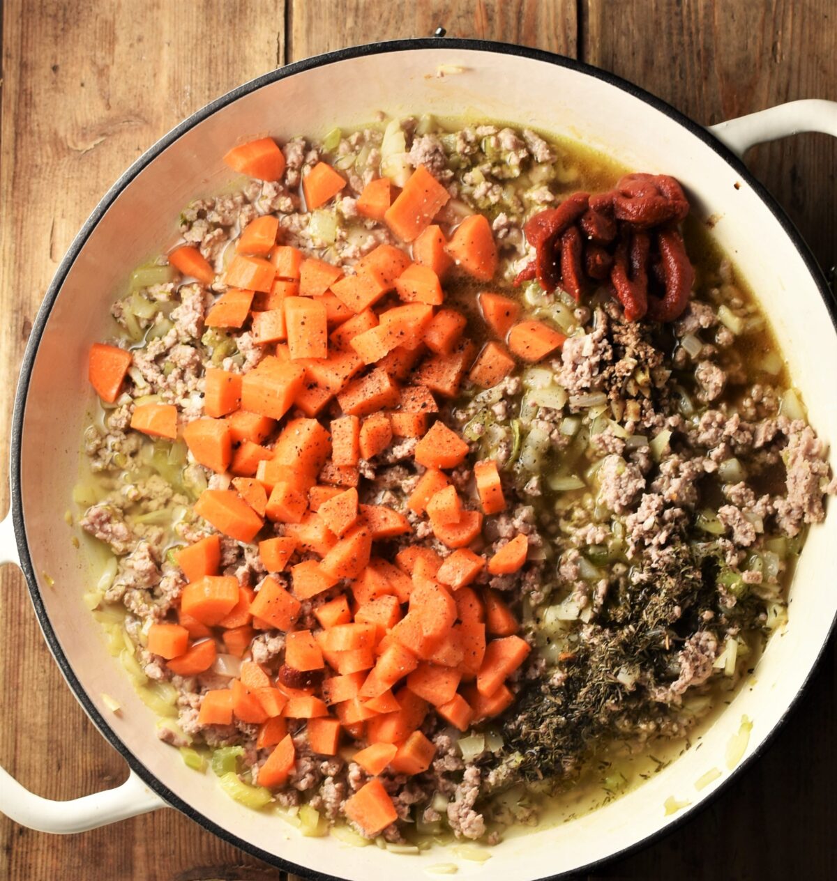 Ground meat, diced carrots, tomato paste and stock in large white shallow dish.