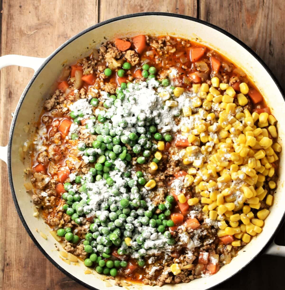 Turkey mince in sauce with corn, carrots, peas and flour over the top on large white shallow dish.