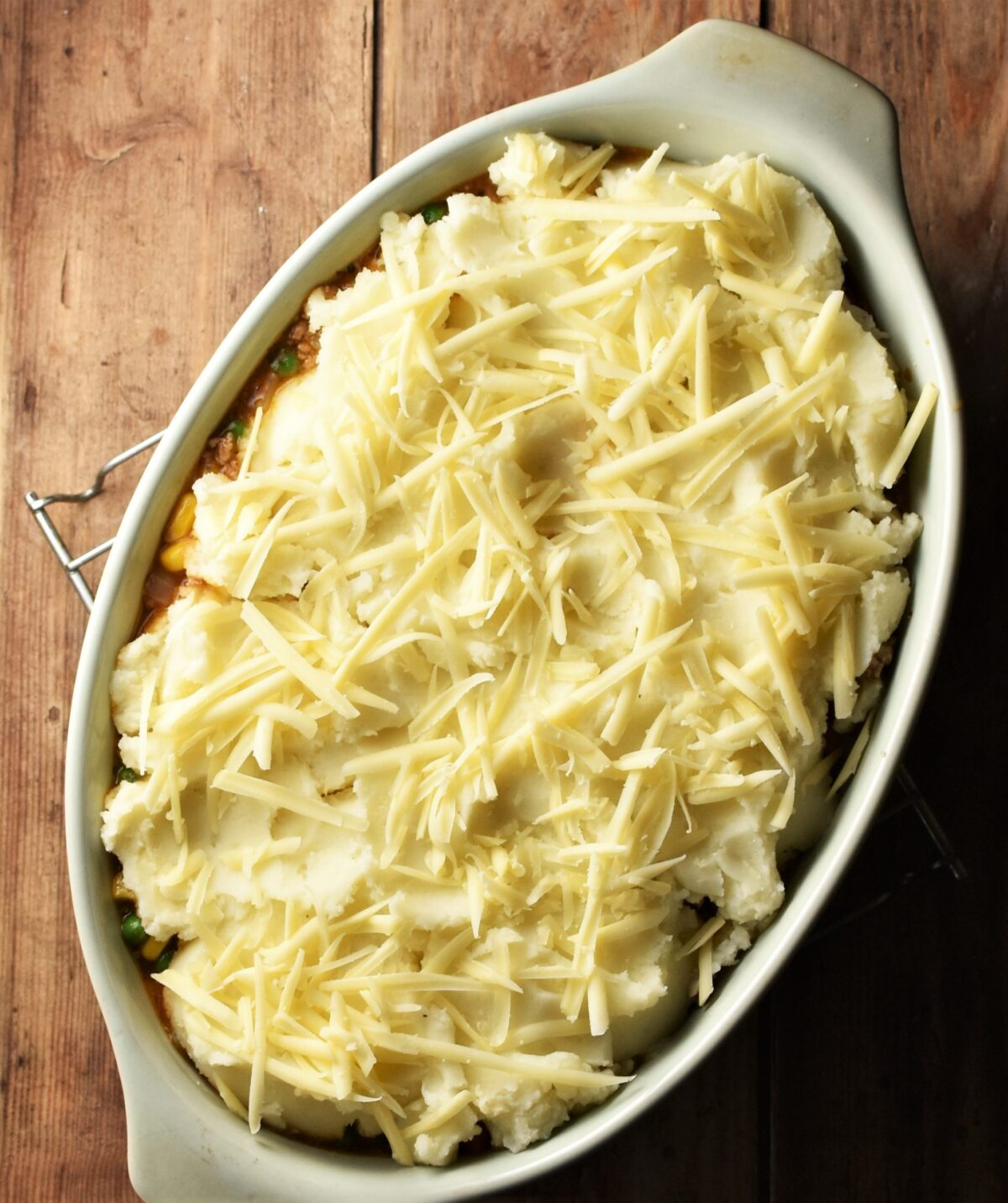 Pie topped with potato mash and grated cheese in green oval dish.