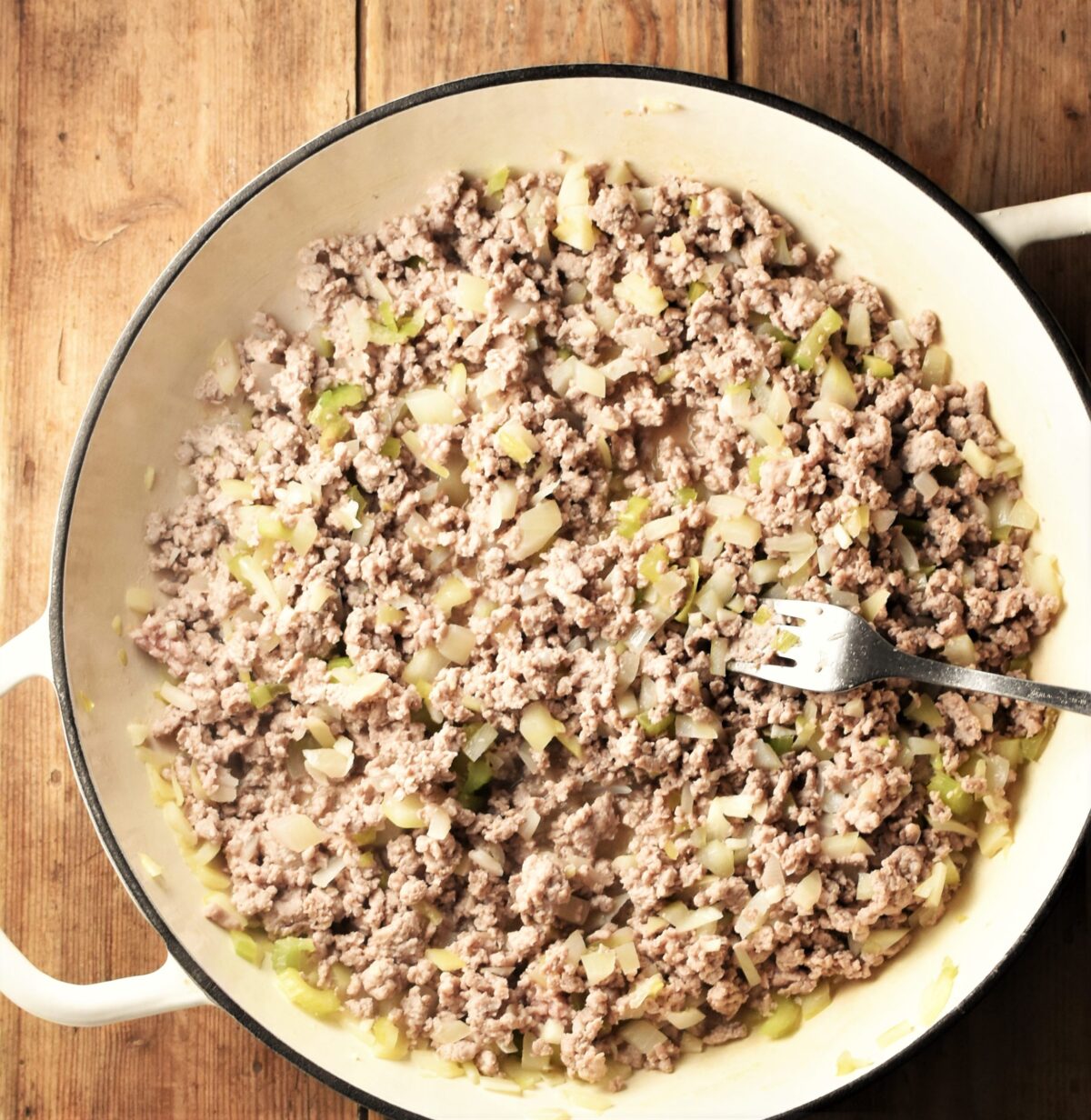 Ground turkey and chopped onions in large shallow white dish with fork.
