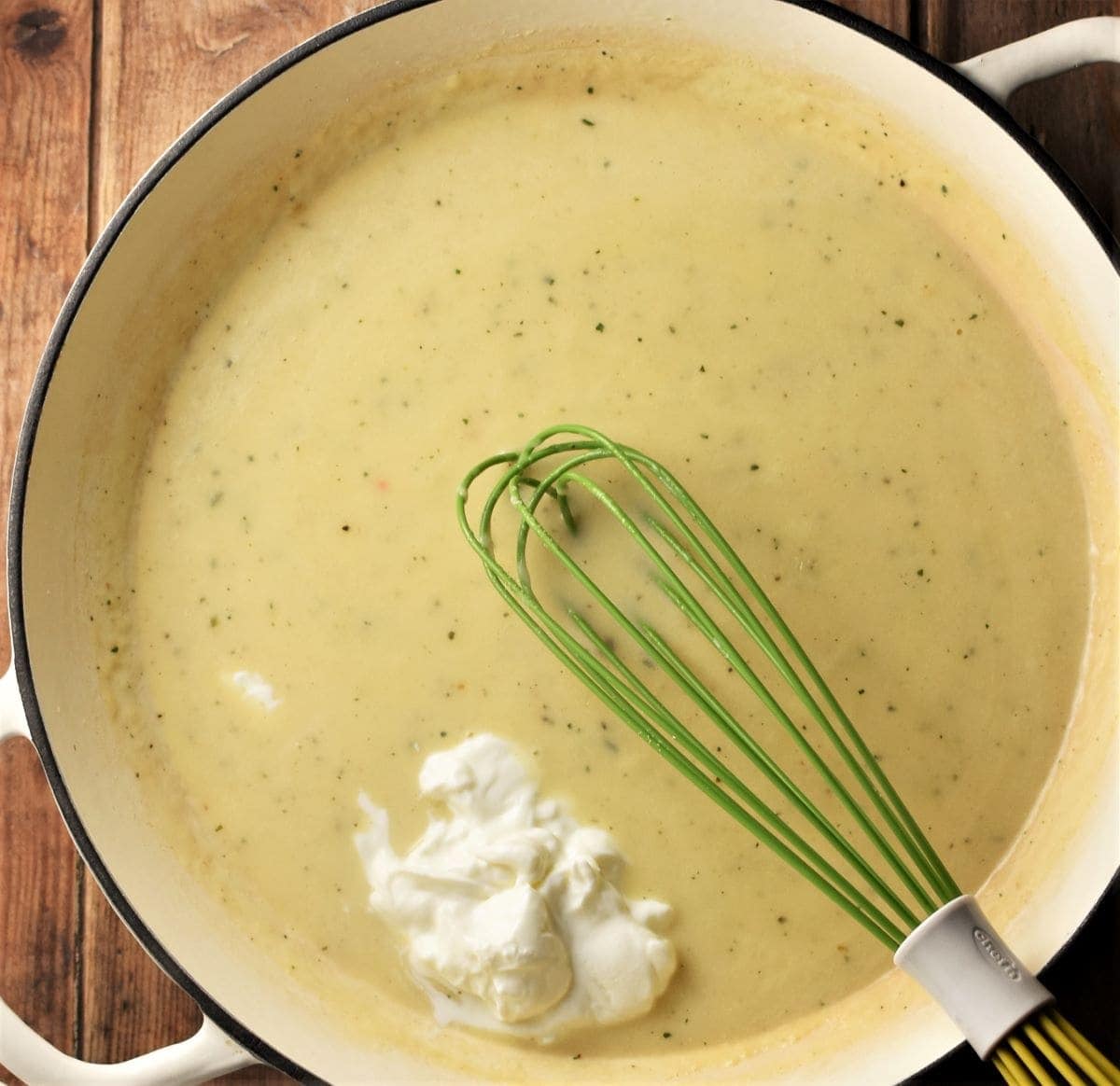 White sauce with fromage frais in large white dish with green whisk.