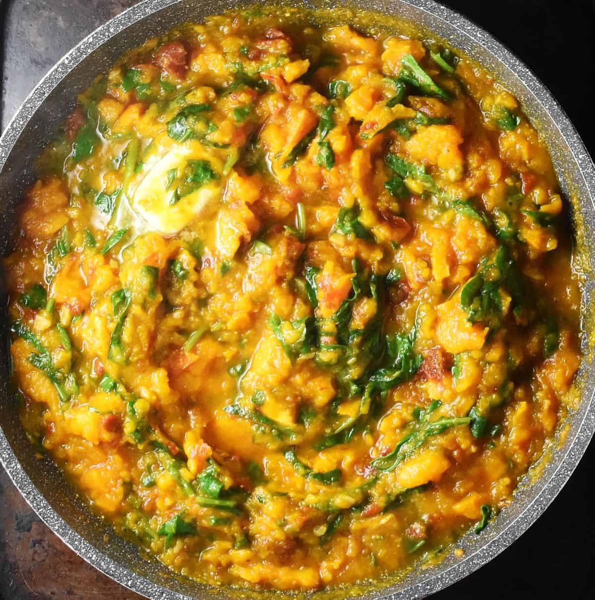 Thick pumpkin pasta sauce with spinach and butter in large pan.
